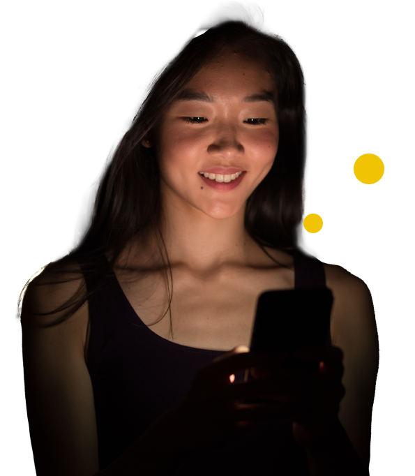 a young asian woman smiling into a mobile phone screen that is illumating her face
