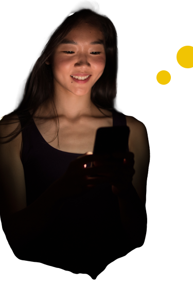 a young asian woman smiling into a mobile phone screen that is illumating her face
