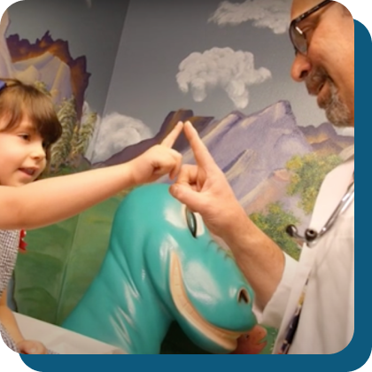 a white doctor wearing a lab coat and stethescope touches his index finger to the index finger of a white five-year-old girl