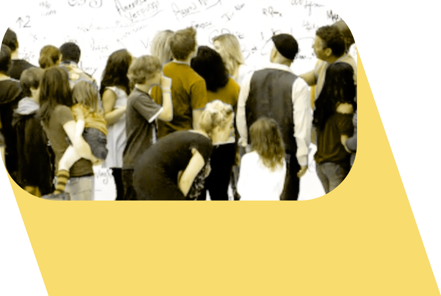 A group of 30 children and adults standing in front of a wall with writing on it