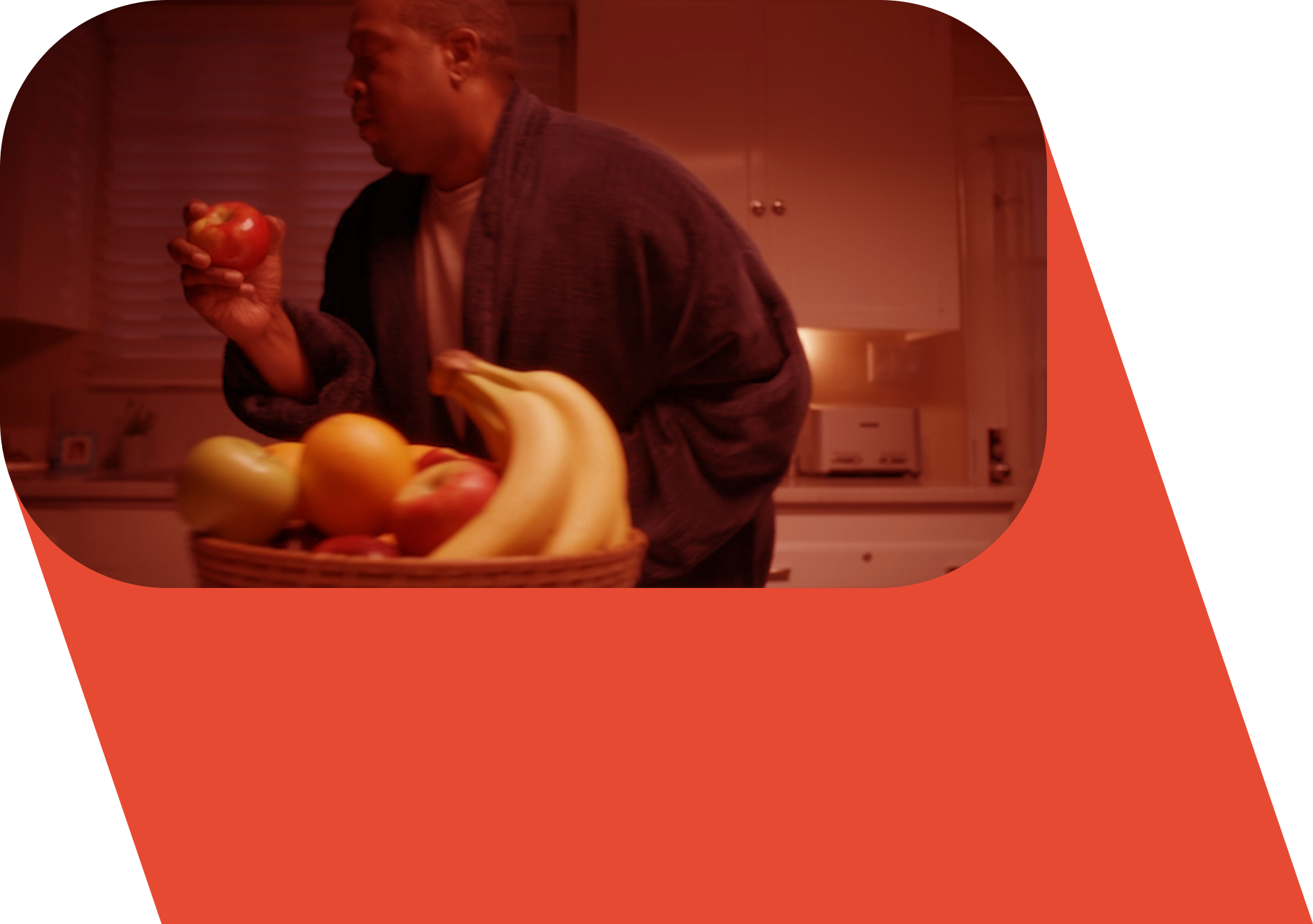 A man in a bathrobe holding an apple, wiht a bowl of fruit next to him