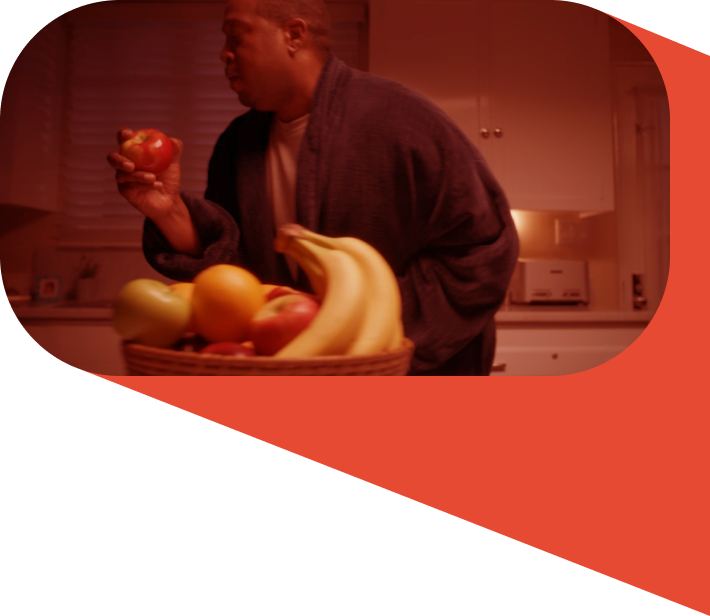 A man in a bathrobe holding an apple, wiht a bowl of fruit next to him