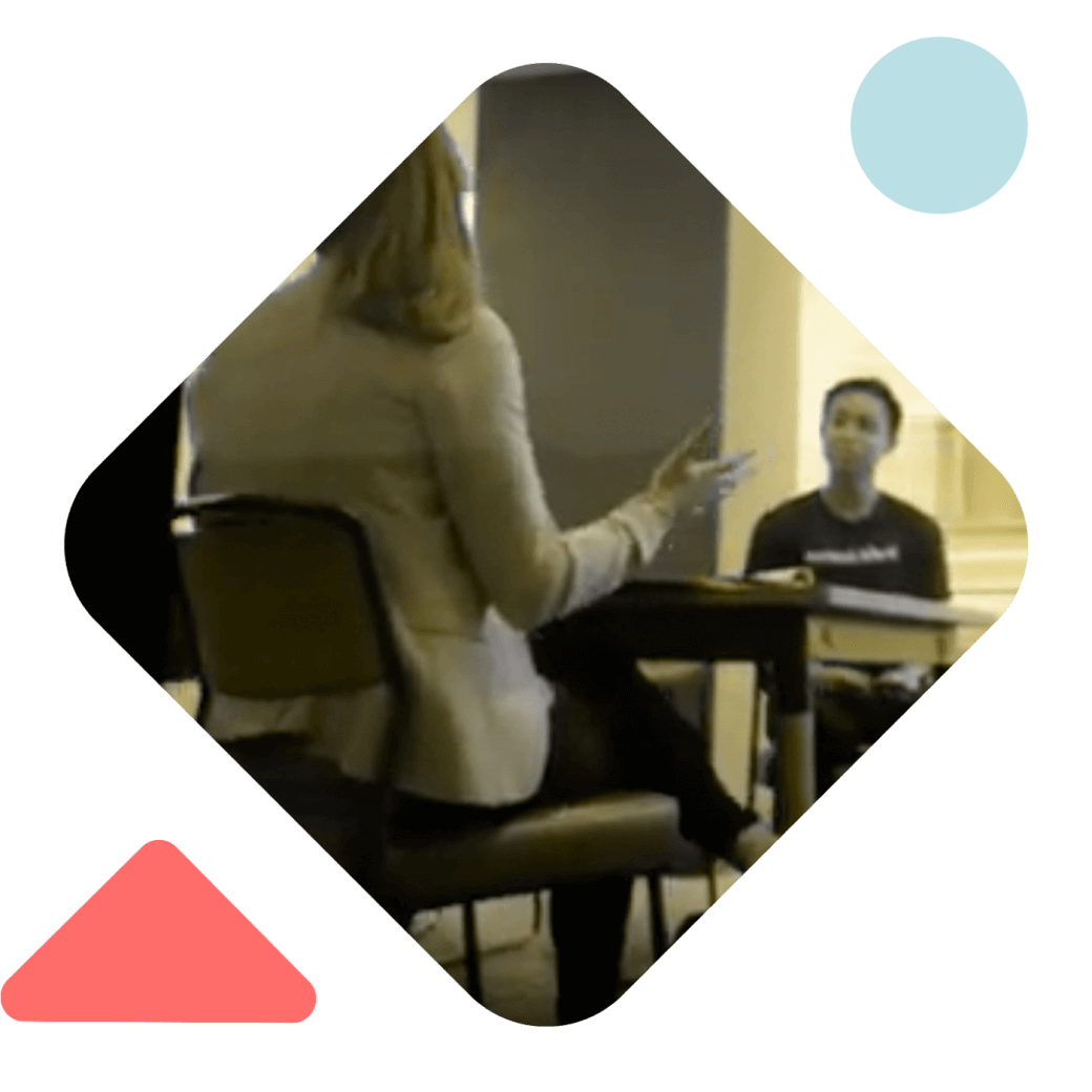 a blonde woman sitting at a table speaks to a person with short hair at the other end of the table