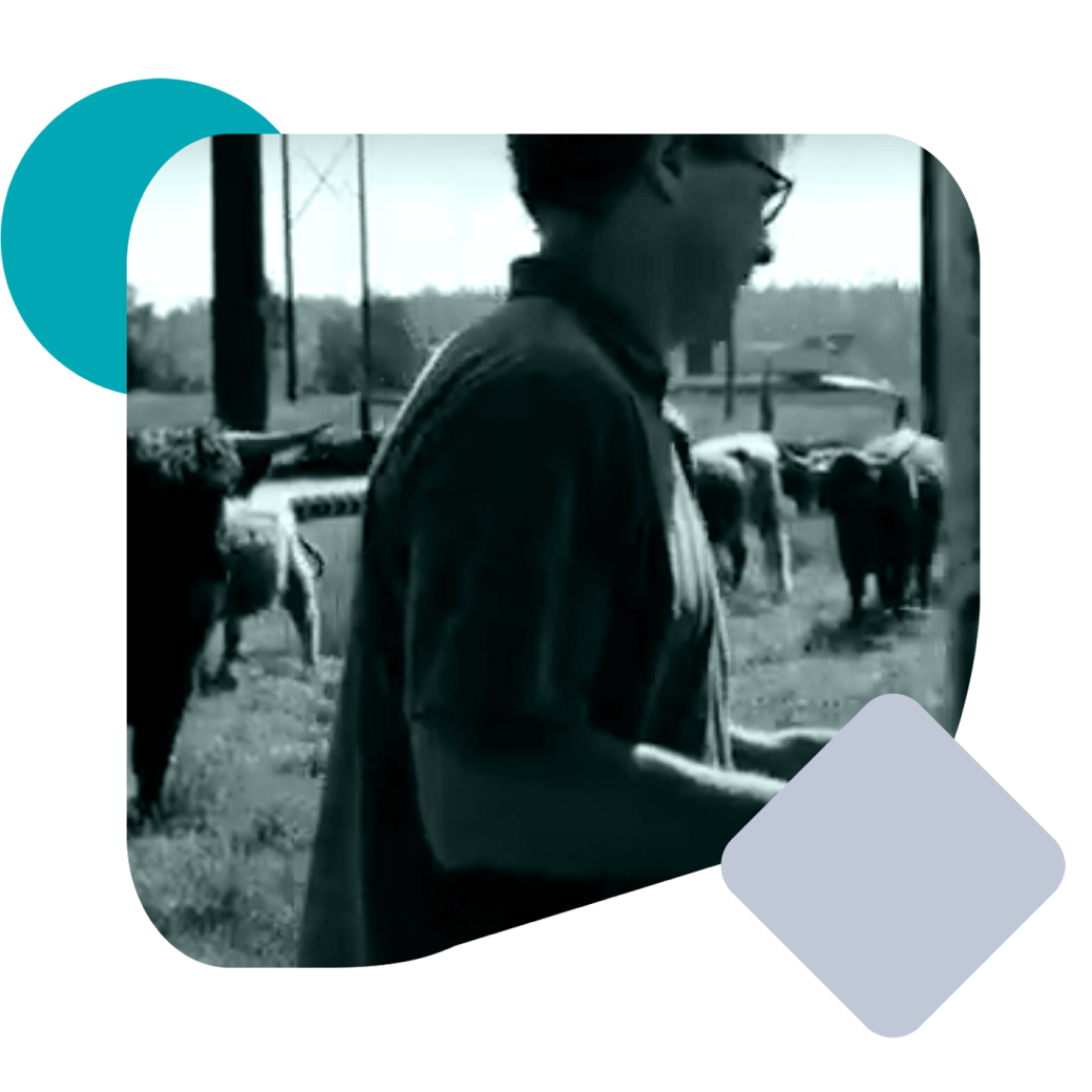 man with glasses on a farm with cattle in the background
